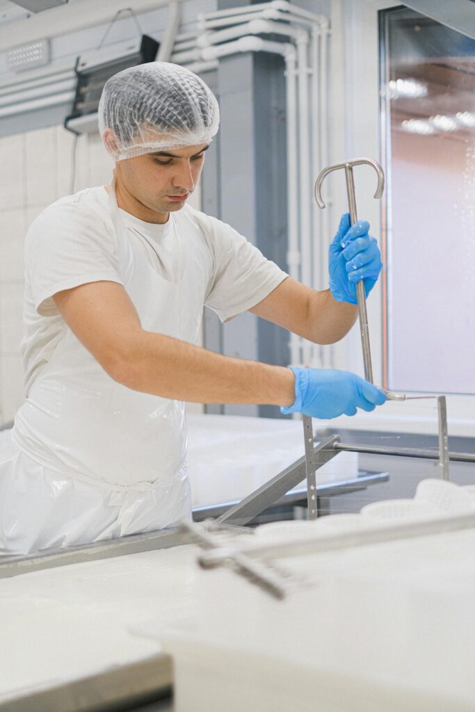 Worker in a cheese factory with protective gear, ensuring hygiene in dairy production setup.
